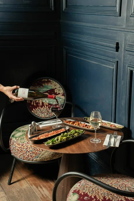 Service du vin à une table ronde garnie de plats, chez Maria Belza